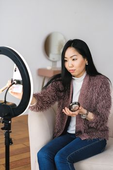 Woman using ring light and smartphone for vlogging at home. Indoor lifestyle setup.