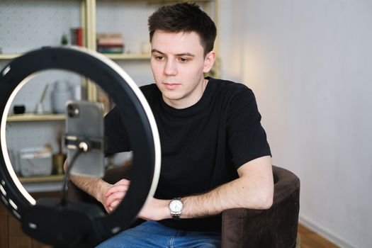 Man sitting indoors with a smartphone and ring light, capturing content at home.