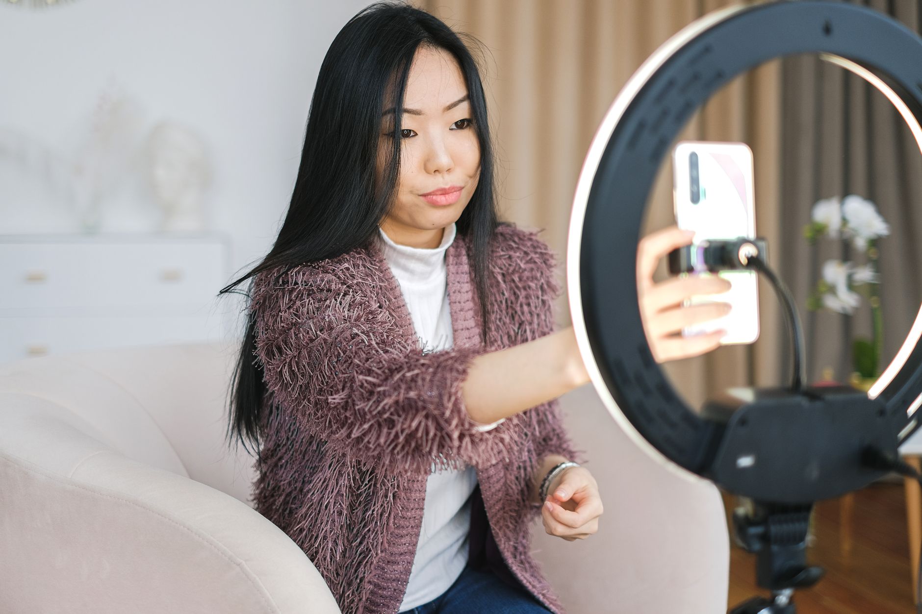 How to Fix Flicker in Phone Videos Under LED Lights Asian woman using smartphone and ring light for vlogging indoors.