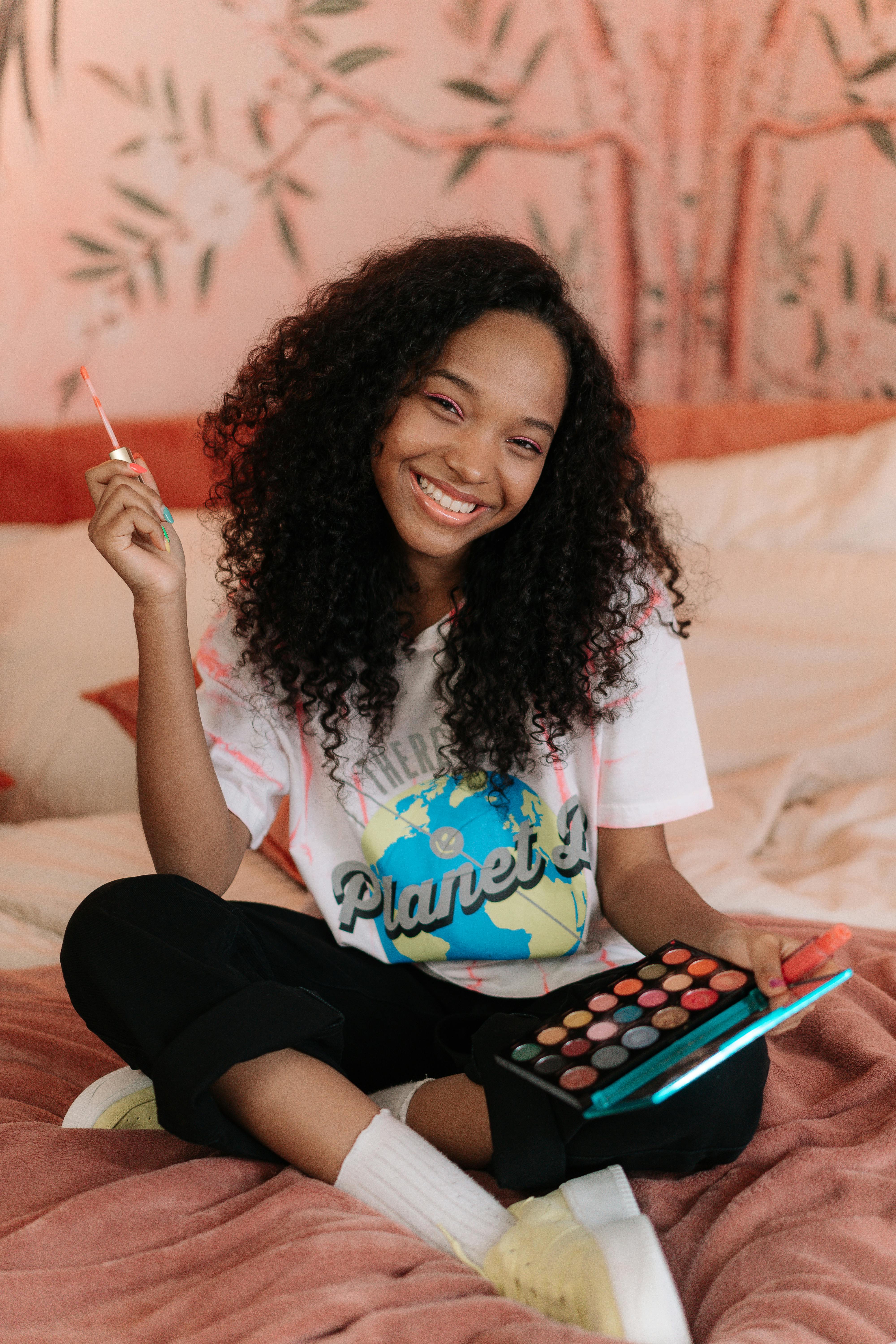 young girl sitting on bed holding a lip gloss