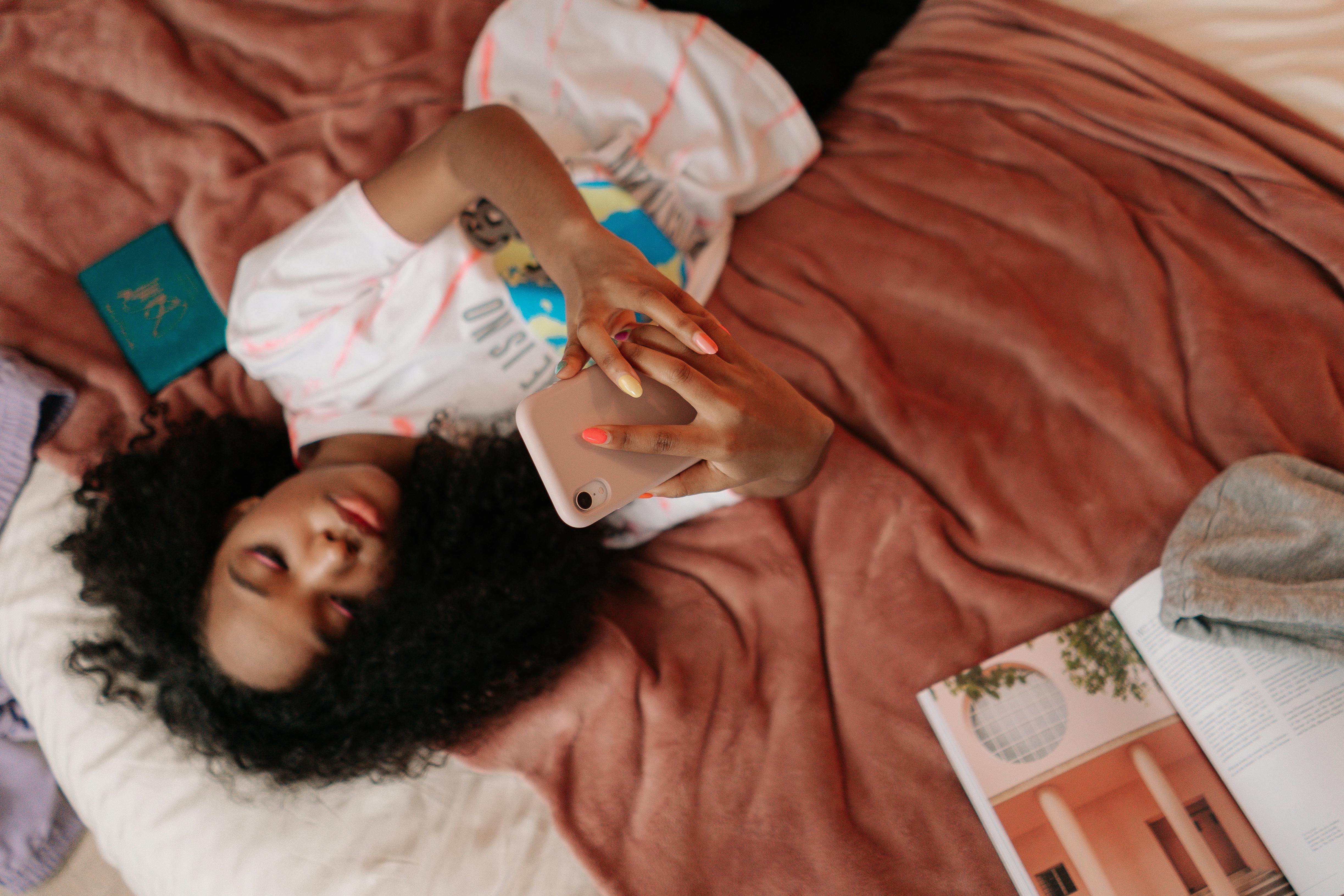 young girl lying on bed holding a cellphone