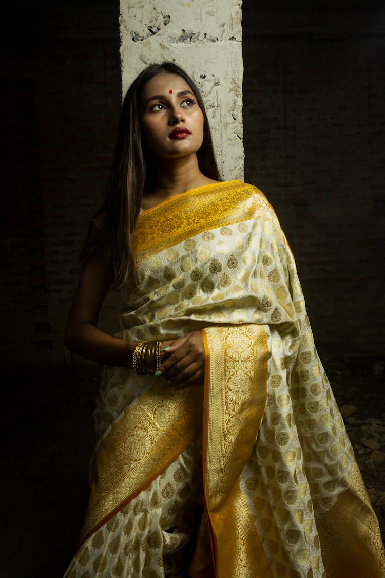 Woman In Yellow And Gold Dress Leaning On Concrete Pole