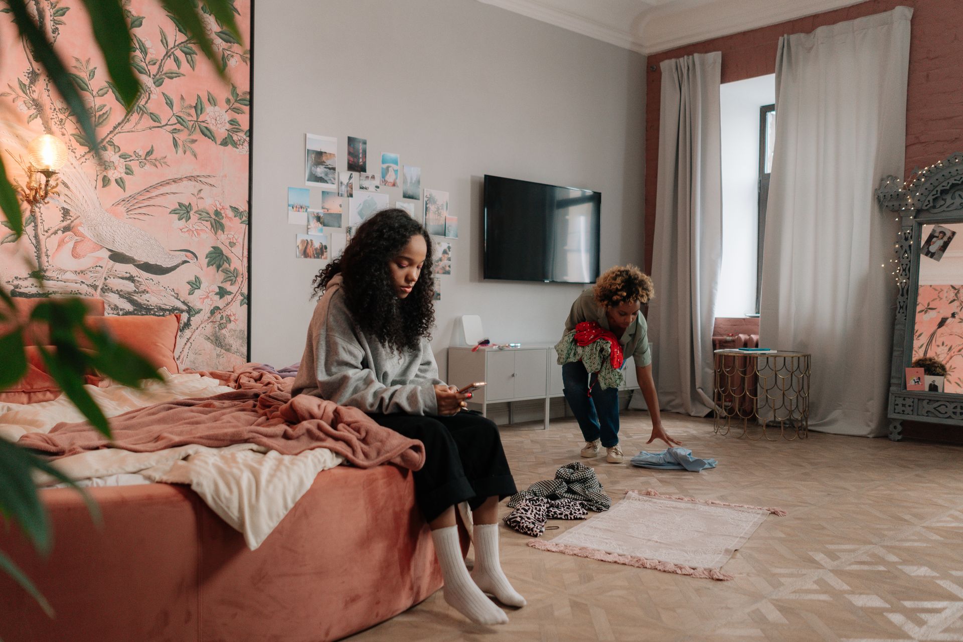 Girl Sitting with Smartphone and Mother Cleaning Room