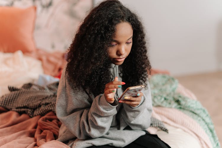 Girl Sitting On Bed Using Cellphone