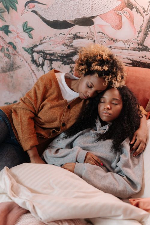 Free A loving mother embraces her sleeping daughter on a cozy bed, surrounded by warm decor. Stock Photo