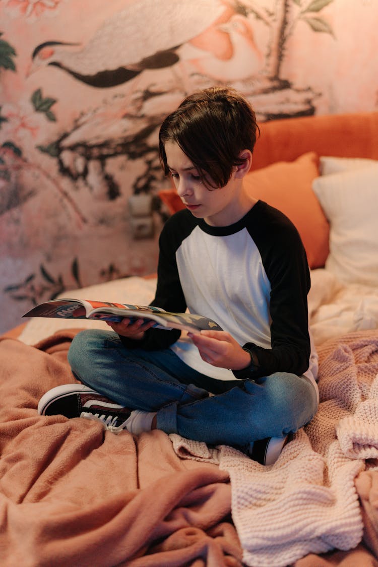 Boy Sitting On Bed Reading A Magazine