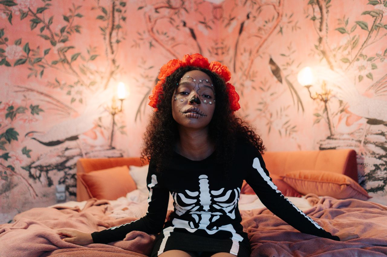a young girl in a skeleton costume sits on a bed adorned with face pai