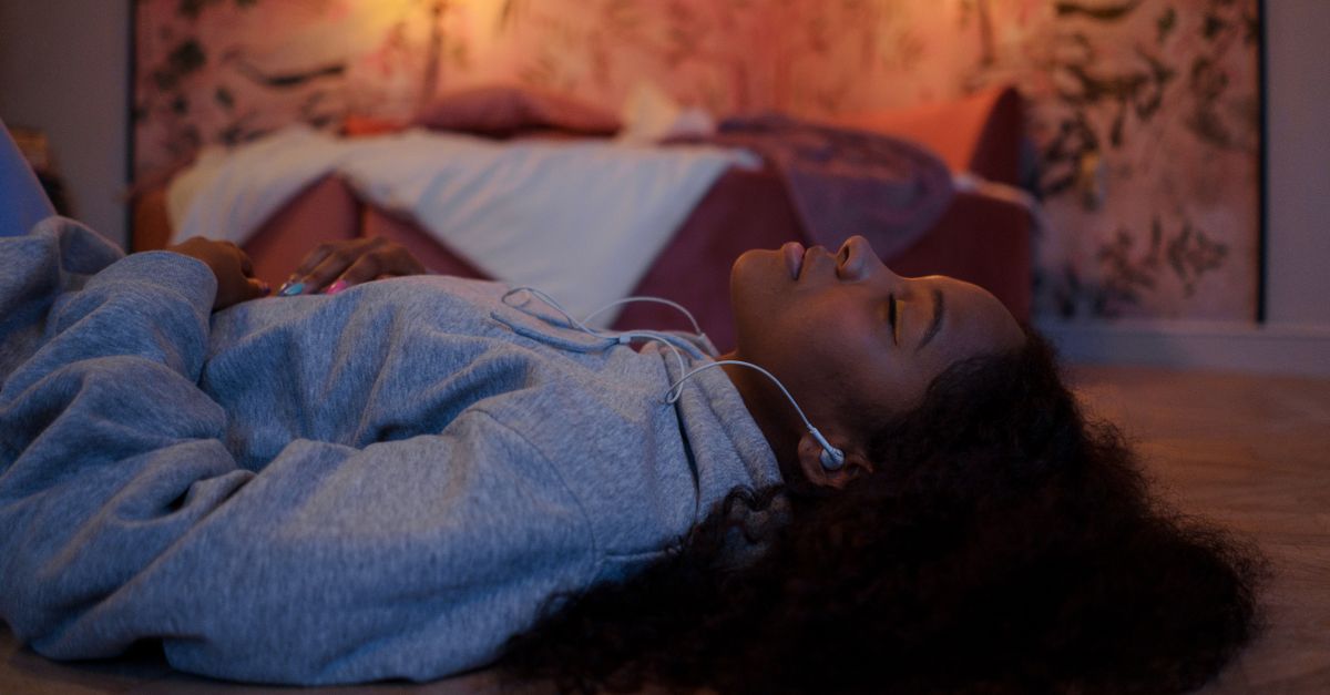 a cozy bedroom with fairy lights, a vinyl player, and a person lying on the floor with eyes closed