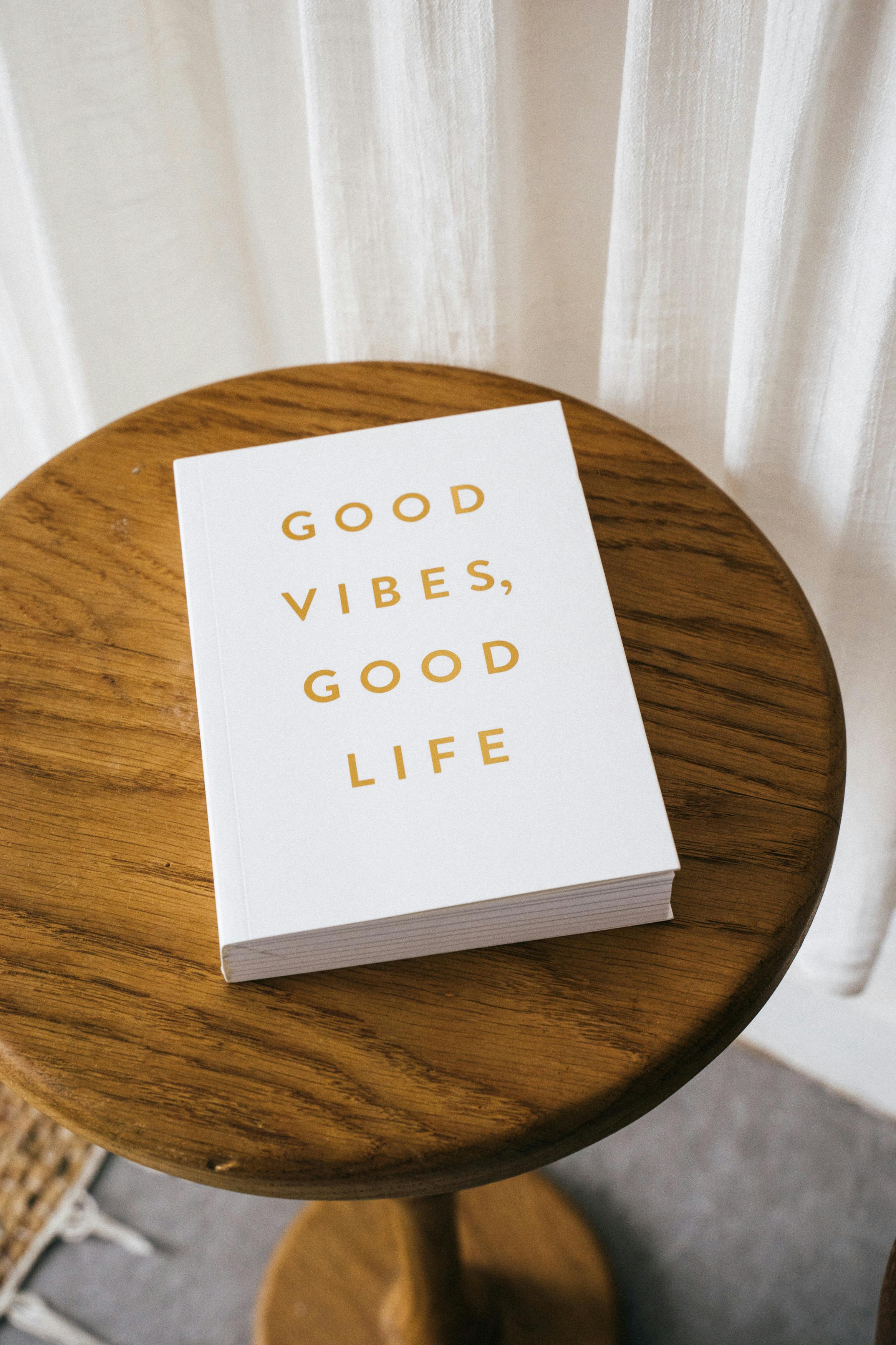 Free A white book titled 'Good Vibes, Good Life' rests on a wooden table in a bright, minimalistic room. Stock Photo
