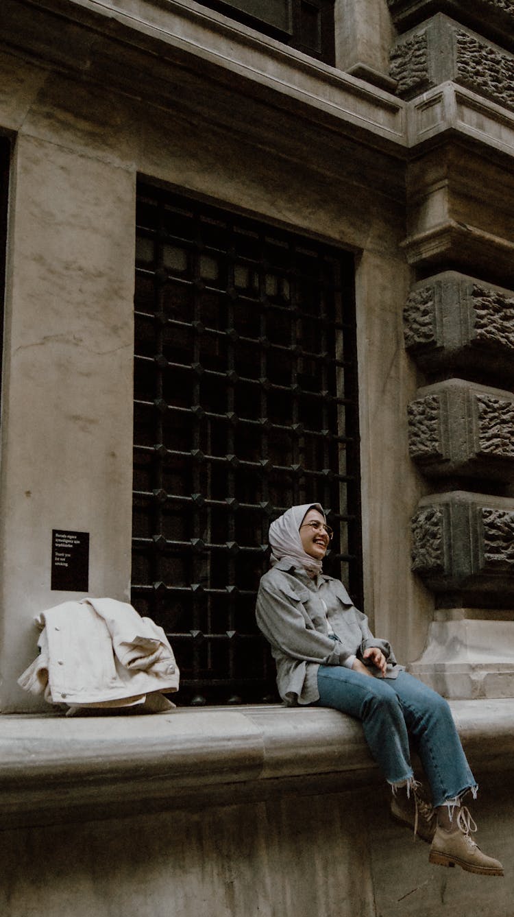 Laughing Hijabi Woman Sitting On Ledge Of Old Building 