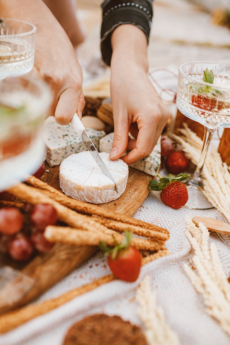 Person Slicing Cheese On Wooden Surface 