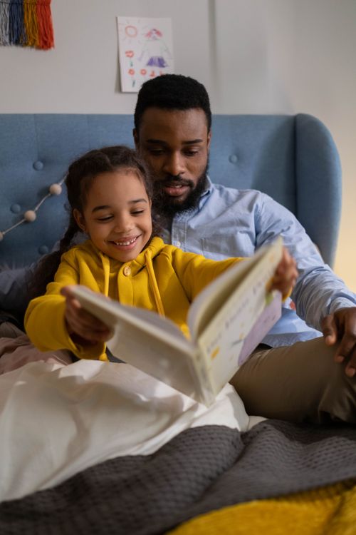 Free A joyful moment of a father and daughter reading together in a cozy bedroom setting. Stock Photo