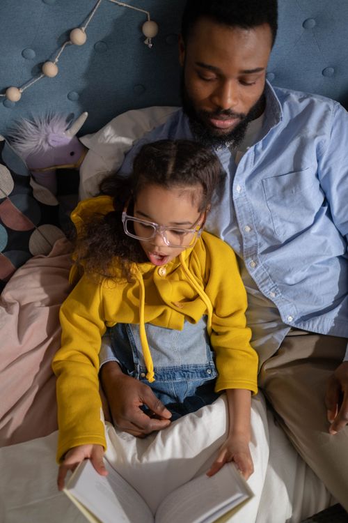 Free A father reading with his daughter in bed, fostering family bonding and learning. Stock Photo