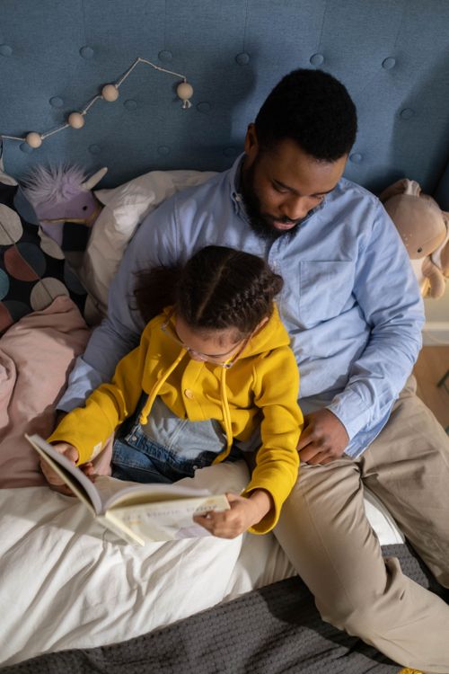 Free A father and daughter share a tender moment reading a book together in a cozy bedroom setting. Stock Photo