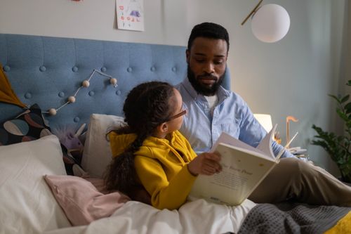 Free A father and daughter share a bonding moment reading together in a cozy bedroom setting. Stock Photo