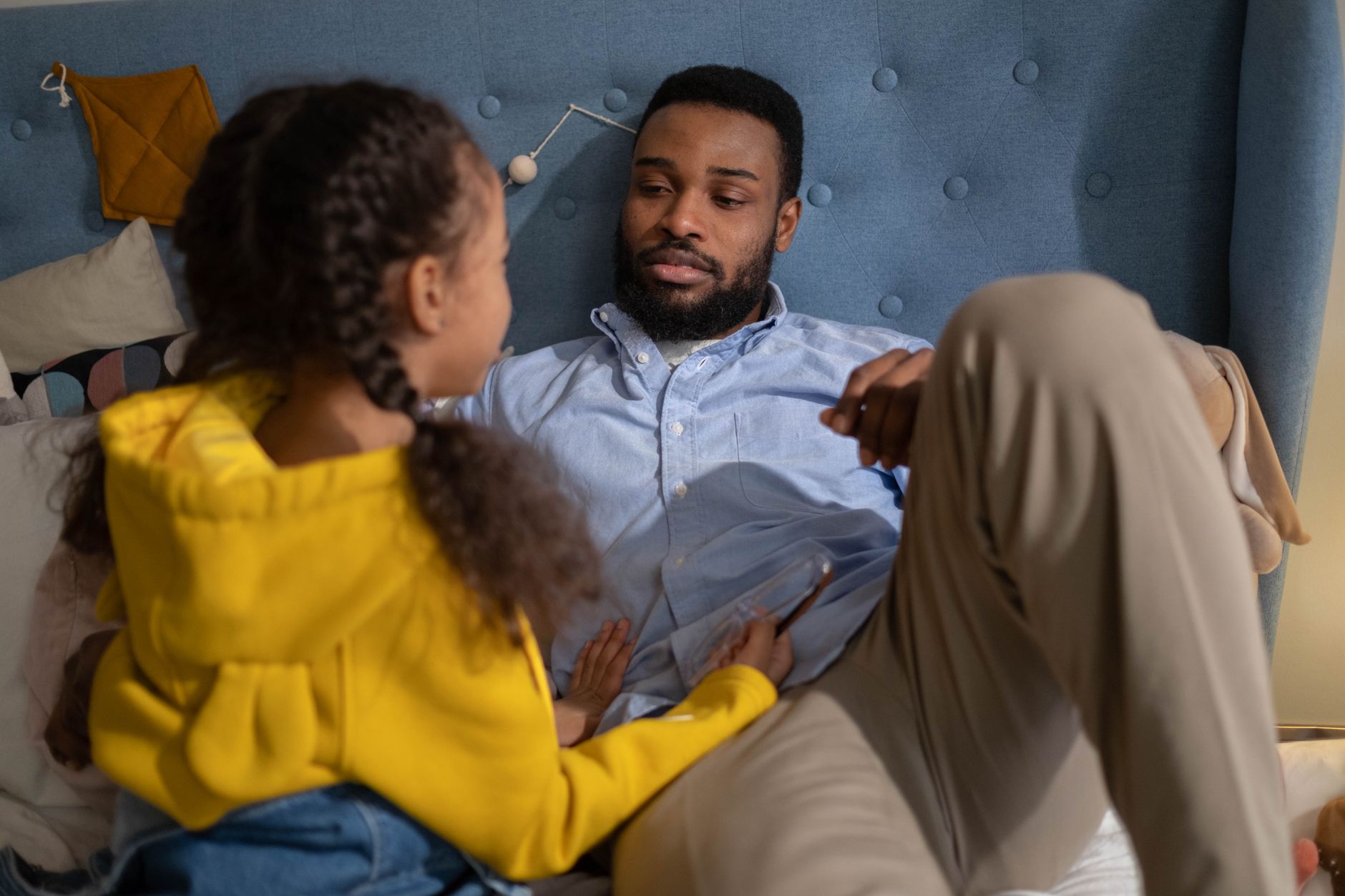 A touching moment between a father and daughter having a conversation in a cozy bedroom setting.
