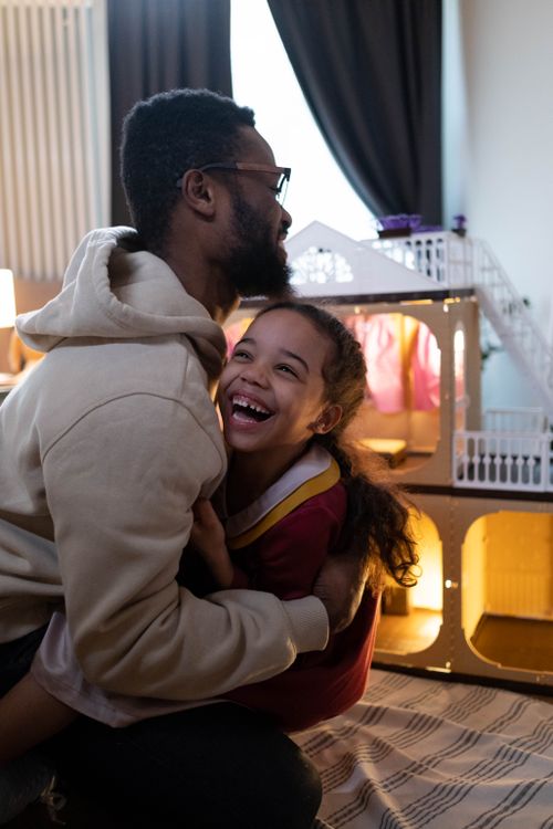 Free A father and daughter share a warm hug in a cozy indoor setting, surrounded by toys. Stock Photo