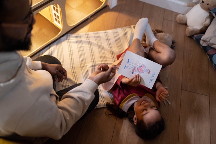 A Happy Girl Holding A Drawing Lying Down On The Floor
