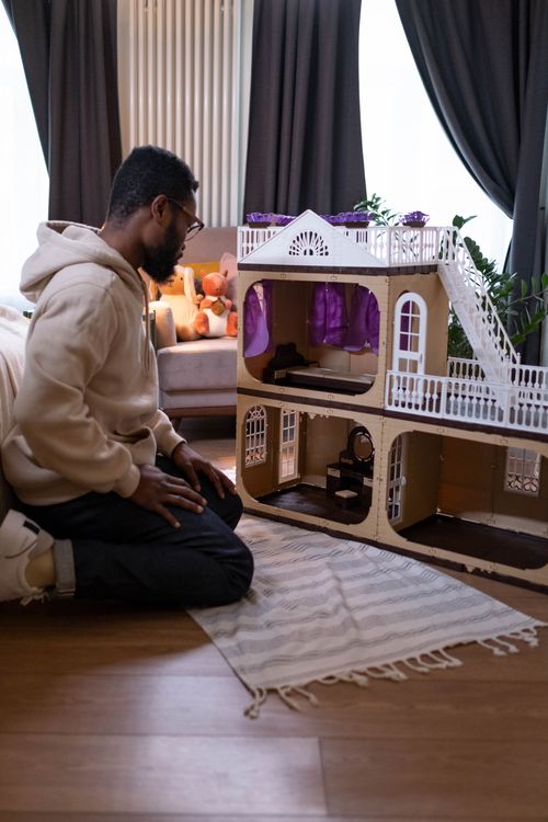 Free A father kneeling and attentively playing with a dollhouse in a cozy room. Stock Photo