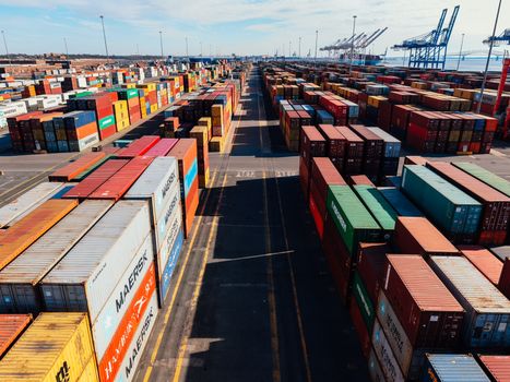 From above of asphalt roadway among large colorful metal containers placed in industrial area under cloudy sky in sunny day