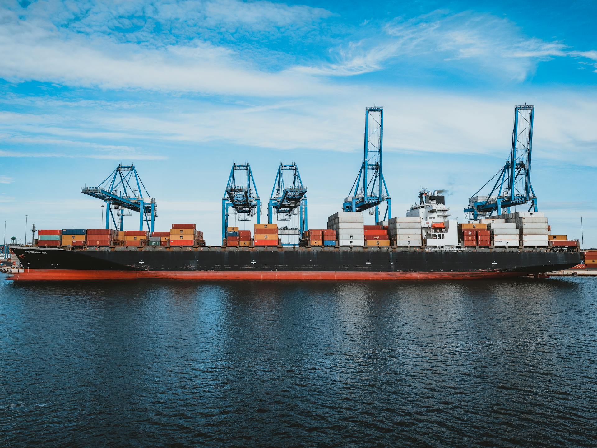Large cargo ship with colorful metal containers floating on rippling water of ocean under cloudy blue sky in daylight