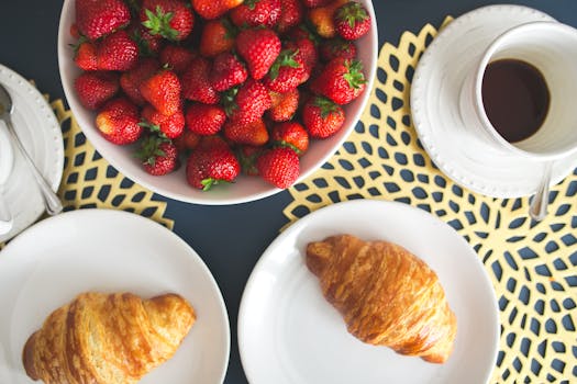 Fresh buttery croissants, hot cup of coffee and bowl with strawberries