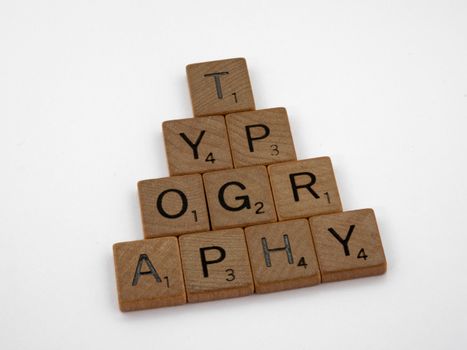 Close-up of wooden Scrabble tiles forming the word typography on a white background.