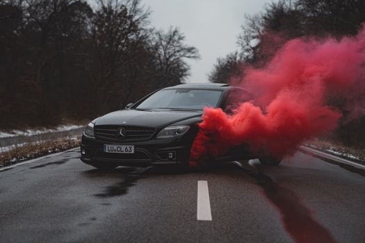 Dynamic shot of a black Mercedes Benz with dramatic red smoke on an empty road.