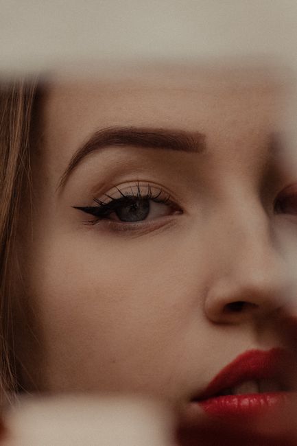Mirror reflection of crop thoughtful young lady with red lipstick and makeup in light room
