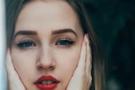 Woman in makeup with hands on face looking at camera