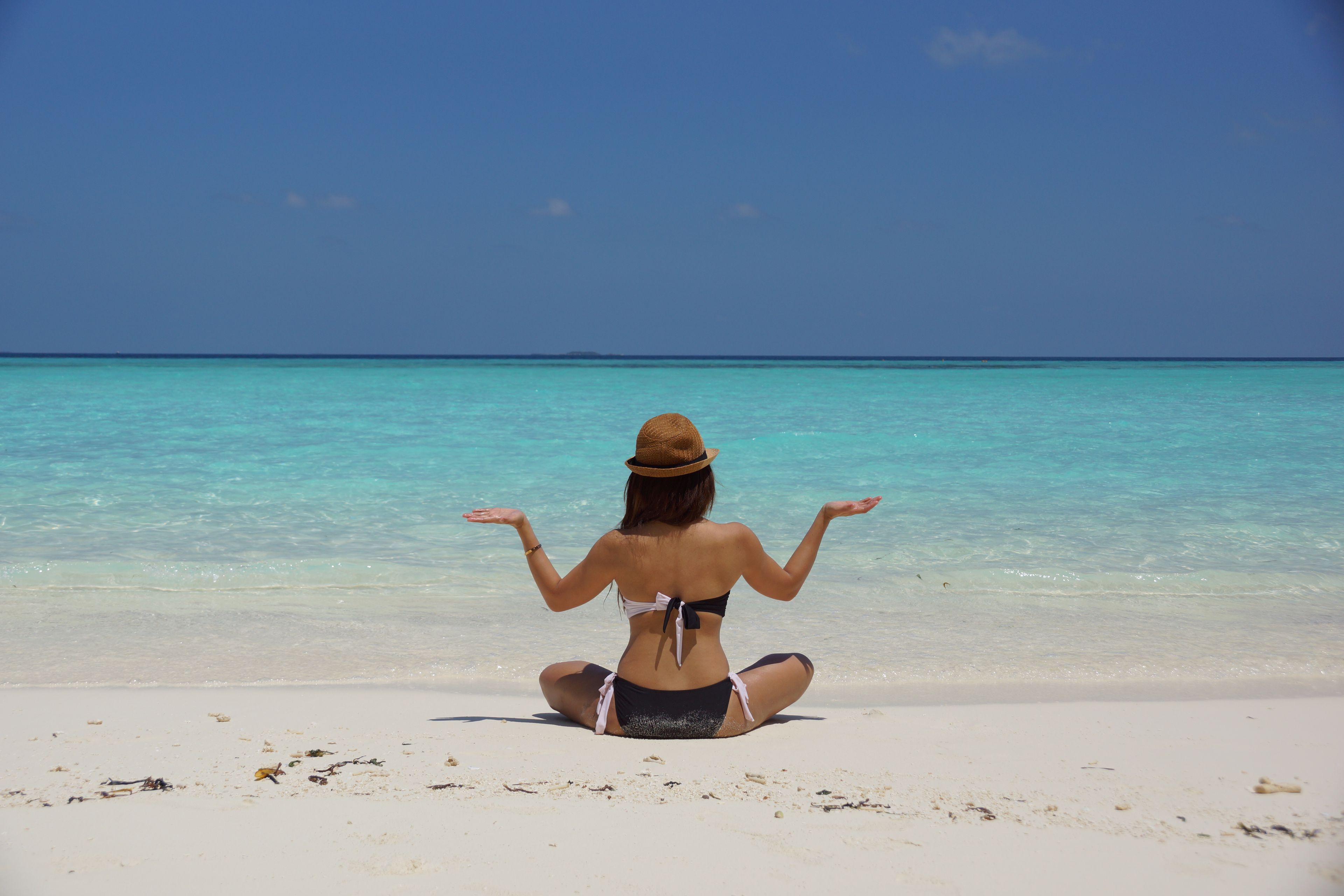 A woman meditating on a serene beach in the Maldives, under a clear blue sky.