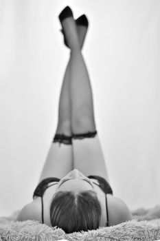 Black and white image of a woman fashion model lying down with legs raised, exuding elegance and style.