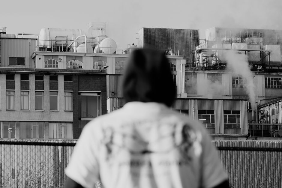 Back view of black and white anonymous male standing on street and looking at industrial building in suburb