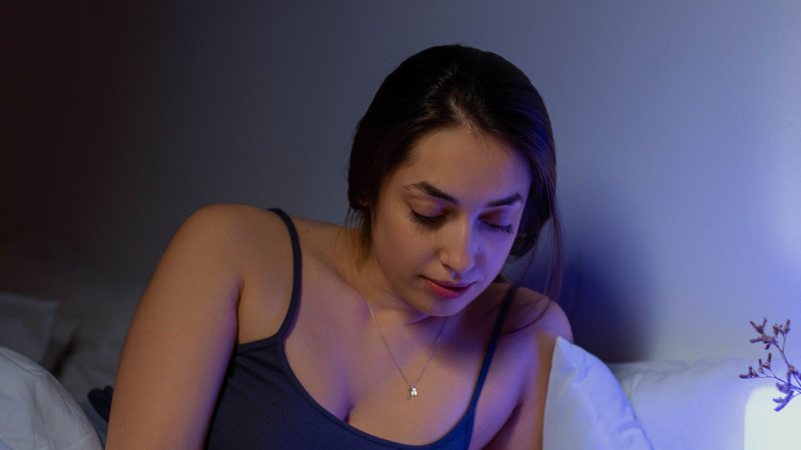 A young woman writing in a notebook in a softly lit bedroom at night