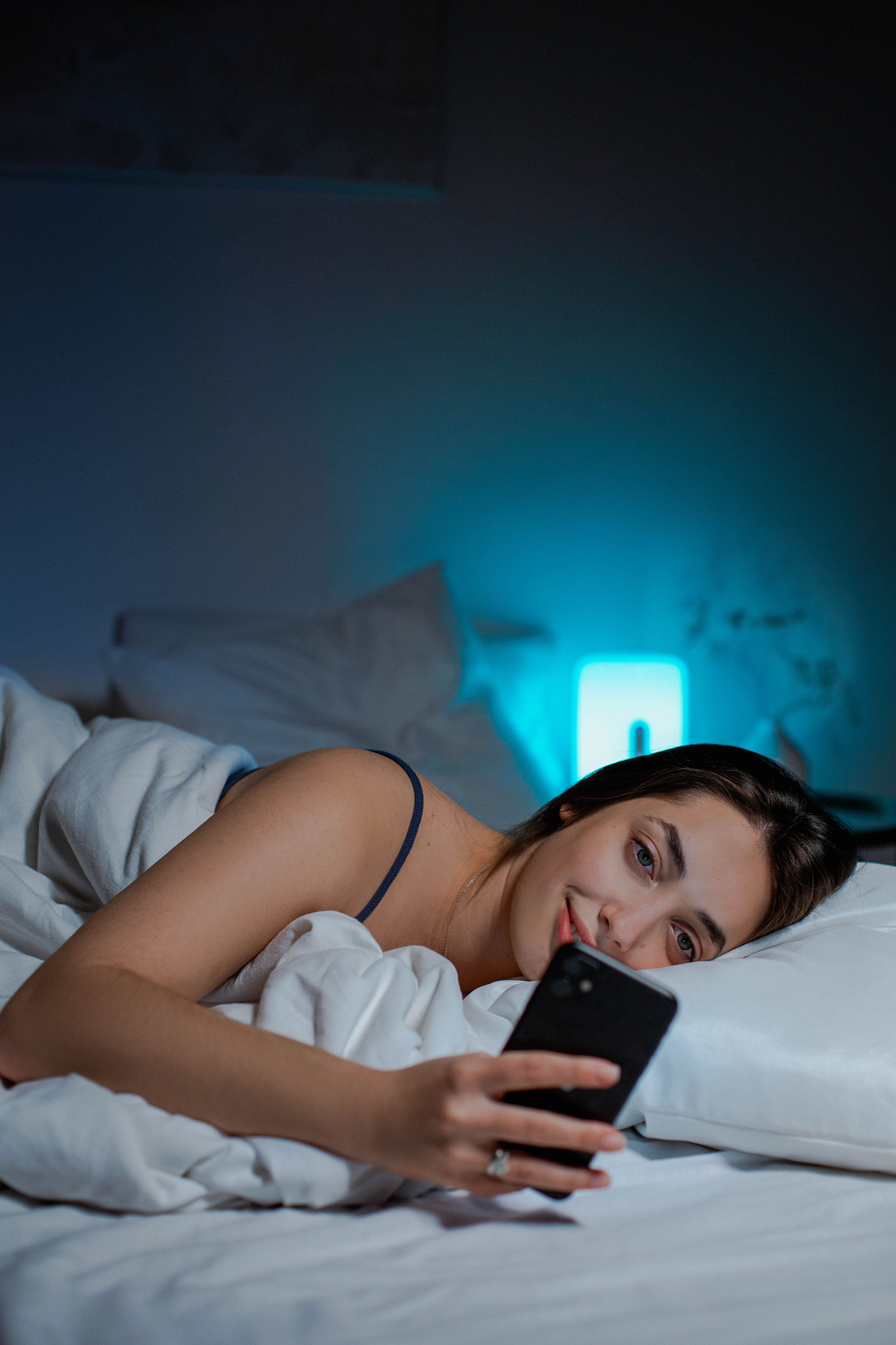 A woman lying in bed at night, typing on her phone