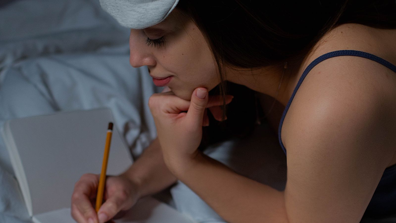 A woman wearing a sleep mask writing in a notebook while lying in bed