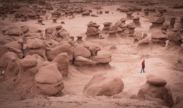A person walks among the eerie, mushroom-shaped rock formations of Goblin Valley State Park, Utah.
