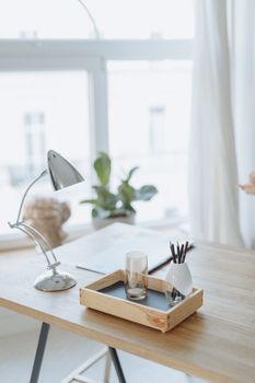 A clean and stylish minimalist workspace featuring a desk lamp, glass, and decorative tray.
