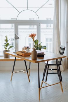 Stylish minimalist workspace featuring a wooden desk with artificial flowers and natural light.