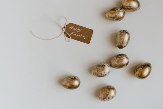 Golden Easter eggs and a 'Happy Easter' tag on a white surface offering copy space.