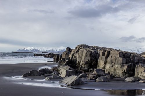 Free Stunning Icelandic beach with dramatic rock formations and snow-capped mountains in the background. Stock Photo
