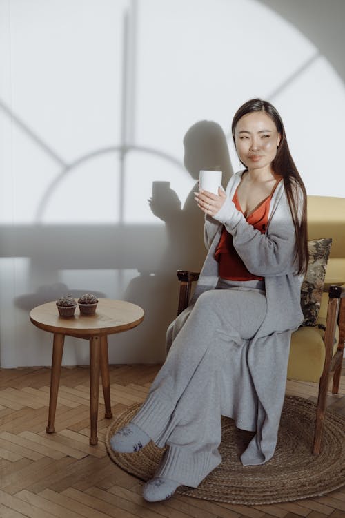 Free A Woman Drinking Coffee while Sitting on a Chair Stock Photo