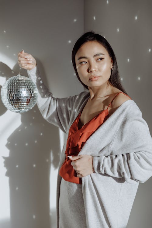 A Woman in Orange Top Holding a Disco Ball