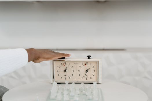 A classic chess clock being pressed by a player during a strategic game indoors.