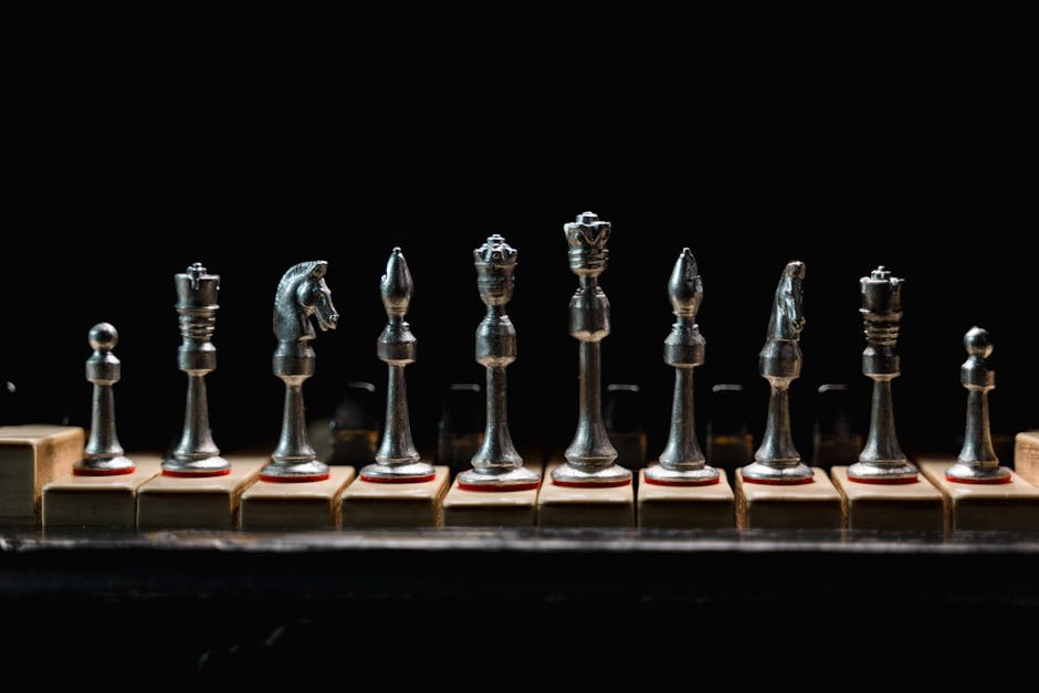 A row of elegant metal chess pieces displayed on wooden blocks against a dark background.