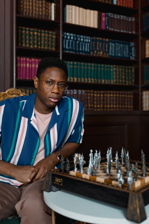 A Man in Striped Polo Shirt Sitting Near the Chessboard while Looking with a Serious Face