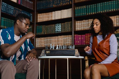 Free Two adults playing chess in a cozy library setting, focused and strategic atmosphere. Stock Photo