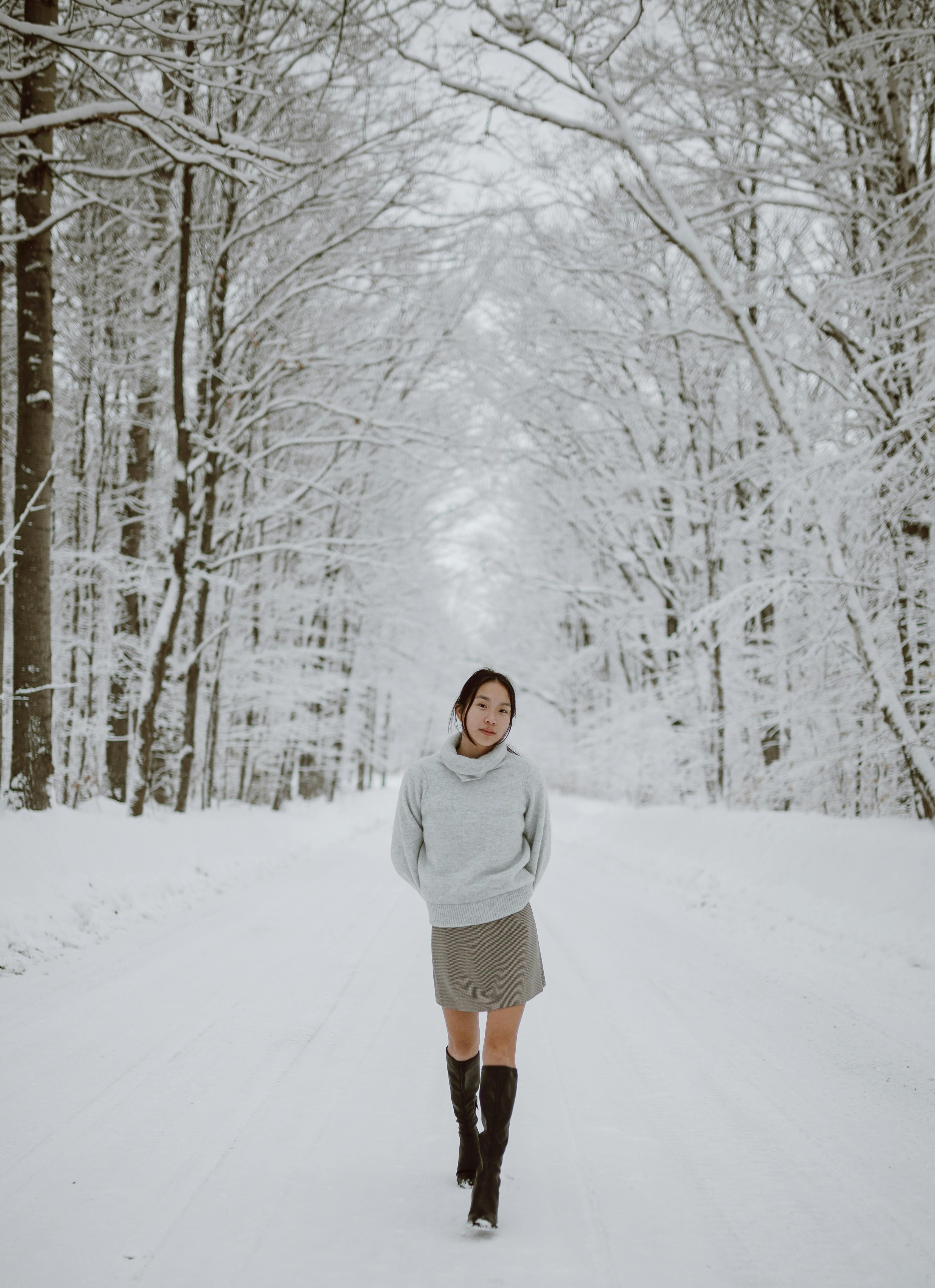 calm young feminine ethnic woman walking in winter forest amidst bare trees