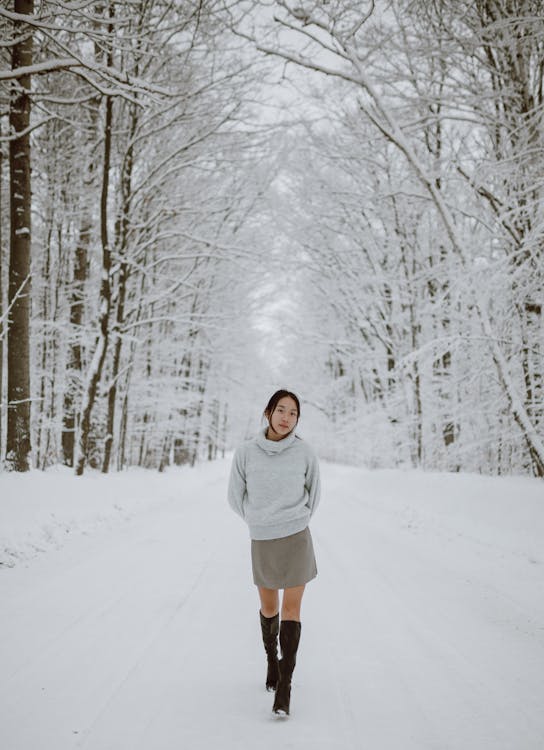 Calm young feminine ethnic woman walking in winter forest amidst bare ...