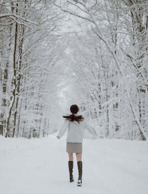 Anonymous female enjoying winter day in forest amidst tall trees covered with snow